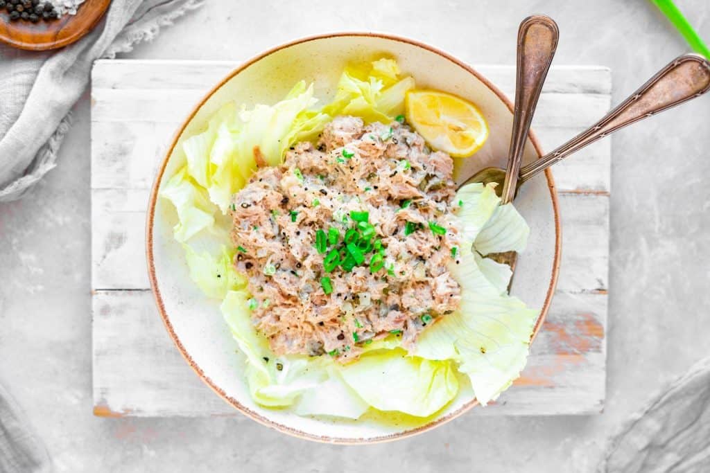 Tuna salad in a bowl over top lettuce leaves and spoon sticking out.